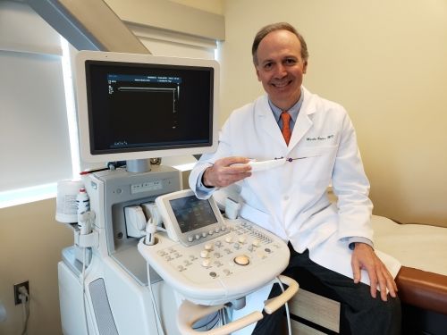 Dr. Marko Bodor sitting next to an ultrasound machine holding UltraGuideCTR medical device.