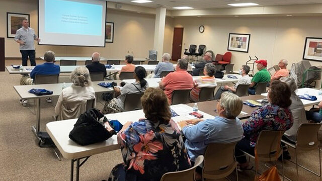 Dr. Perry speaking and presenting a carpal tunnel release presentation in front of a group of patients sitting in a meeting room. 
